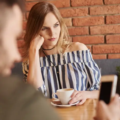 Eine Frau sitzt gelangweilt da und trinkt einen Kaffee.