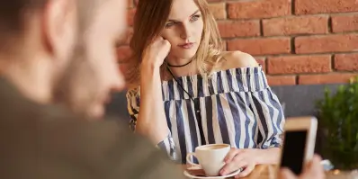 Eine Frau sitzt gelangweilt da und trinkt einen Kaffee.